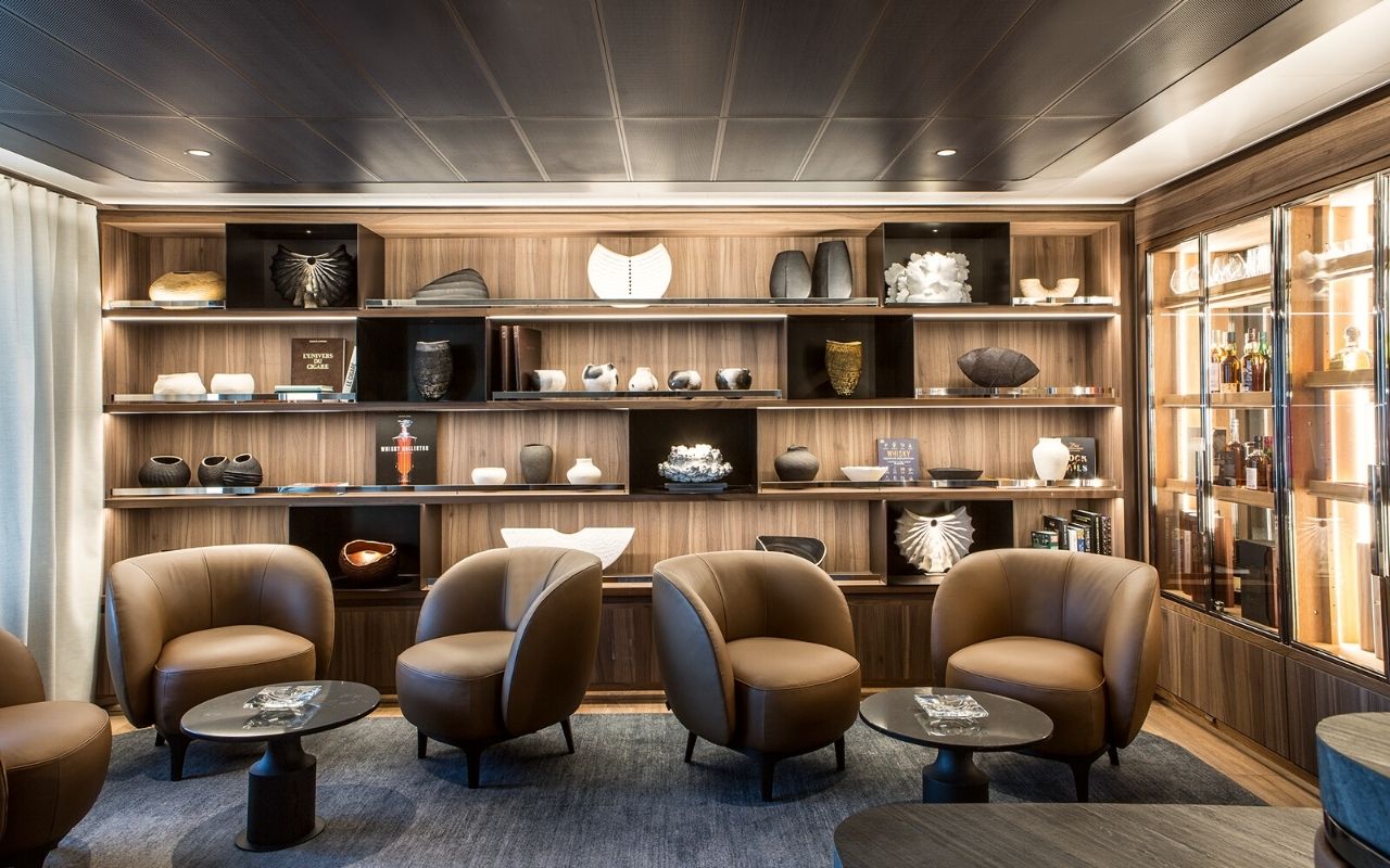 Cigar lounge with leather armchairs and large shelves decorated with art objects from the luxury polar cruise ship Le Commandant Charcot designed by the interior design studio jean-philippe nuel